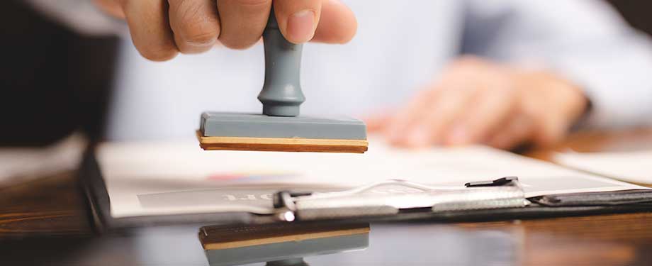 Qual a diferença entre bid bond e performance bond? Na imagem, vemos pessoa carimbando documento em representação a diferença dos dois tipos de seguro, que possuem funções diferentes no processo de licitação