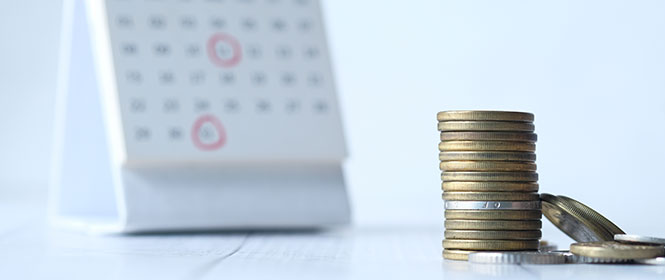 Como funciona o pagamento do seguro adiantamento de pagamento? Na imagem, moedas e calendário representam pagamento adiantado em seguro garantia