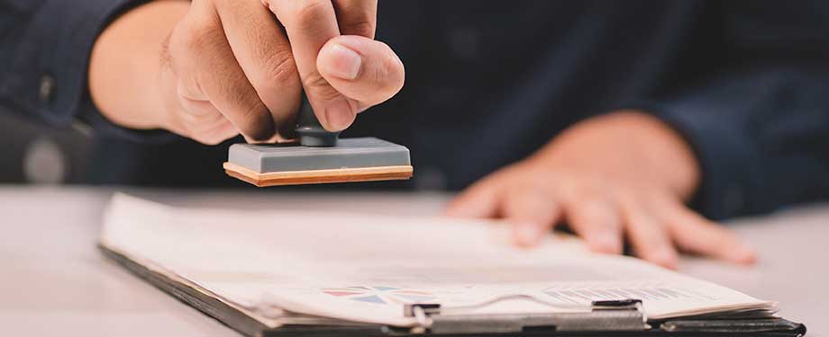 Como o preço do seguro garantia é afetado pelo valor do contrato? Na imagem, homem carimbando contrato de seguro, cuja a garantia depende do valor do negócio fechado