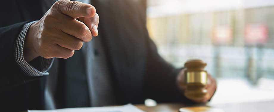 O que é garantia de proposta na licitação? Na imagem, vemos pessoa segundo um martelo da justiça com uma mão e apontando com a outra, representando a importância do seguro garantia licitação para cumprimento das obrigações contratuais