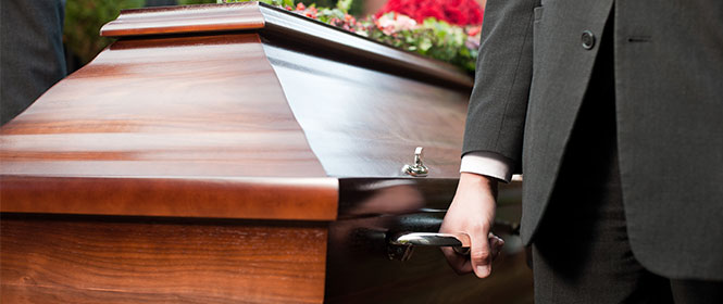 Quem tem direito ao seguro funeral? Na imagem, homem perto de caixão de familiar que faleceu
