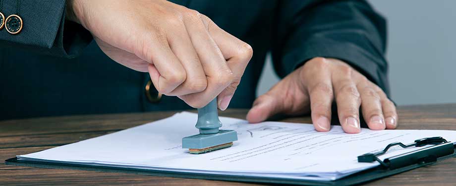 Quem pode participar de licitação? Na imagem, homem carimbando documento em alusão ao que uma empresa precisa para participar de licitação, como seguro bid bond