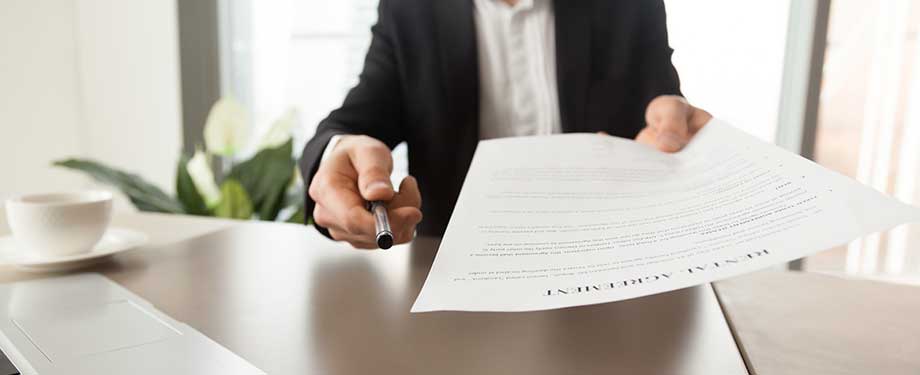 Como funciona o seguro garantia? Na imagem, corretor entregando contrato e caneta para cliente fechar seguro garantia