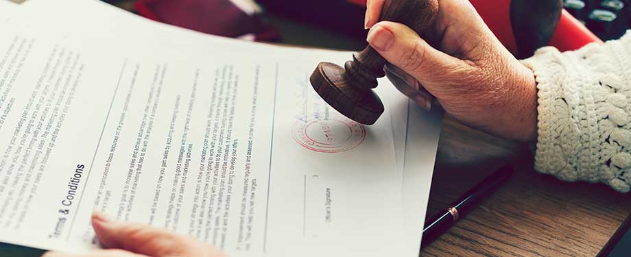 Quais são as vantagens do seguro garantia caução? Na imagem, pessoa carimbando contrato de seguro caução, que tem a segurança como uma das principais vantagens