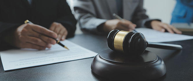 Como funciona o seguro garantia licitante? Na imagem, martelo da justiça e homens assinando contrato em alusão à contratação de seguro garantia