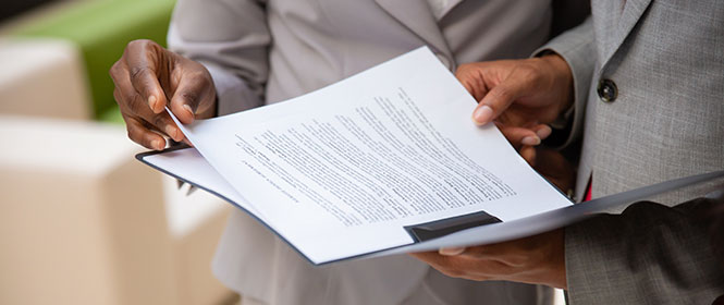 Qual é a documentação necessária para a contratação de seguro garantia licitante? Na imagem, corretor e dono de empresa lendo contrato de seguro garantia licitação