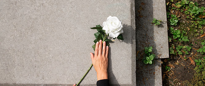 Quanto custa um seguro funeral? Na imagem, mulher colocando rosa em túmulo, evidenciando a importância de um seguro funeral para cobrir o ocorrido